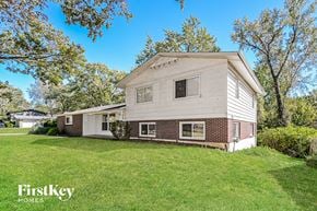 Florissant house for rent - A house with a white exterior and a brick chimney is surrounded by a green lawn and trees.