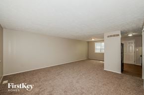 Indianapolis house for rent - A spacious empty room with a carpeted floor and a door on the right side.