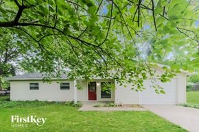 Indianapolis house for rent - A white house with a red door is surrounded by greenery.