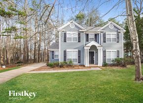 Charlotte house for rent - A house with a grey facade is surrounded by trees and has a well-manicured lawn.