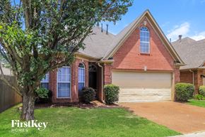 Cordova house for rent - A red brick house with a white garage door and a tree in front.