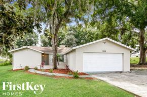Lakeland house for rent - A white house with a garage is surrounded by greenery and has a tree in front of it.