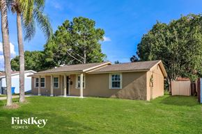 Tampa house for rent - A house with a brown roof and a beige wall is surrounded by a green lawn and trees.