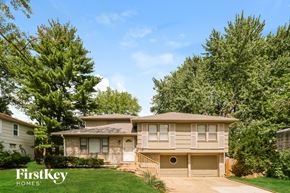 Kansas City house for rent - A house with a brown roof and a white door is surrounded by green trees.