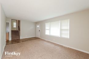 Kansas City house for rent - A spacious empty room with a carpeted floor and a staircase leading to another room.