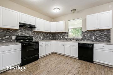 Baytown house for rent - a kitchen with white cabinets and black appliances