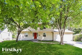Overland Park house for rent - A white house with a red door is surrounded by green trees.