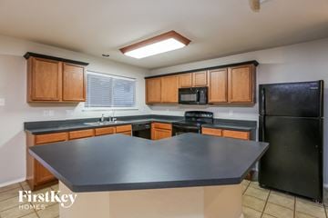 Fort Worth house for rent - a kitchen with black countertops and wooden cabinets and a black refrigerator
