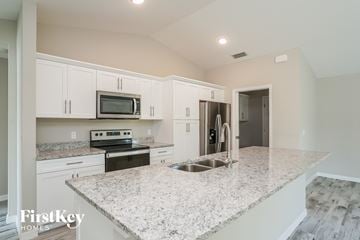 Fort Myers house for rent - a kitchen with white cabinets and a marble counter top