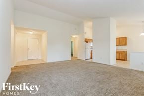 Avon house for rent - A spacious, empty room with a carpeted floor and white walls, with a door on the left and a kitchenette on the right.