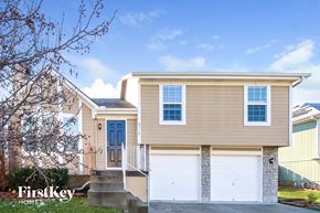 Kansas City house for rent - A two-story house with a blue door and garage doors is for sale by FirstKey Homes.