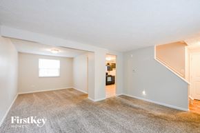 Indianapolis house for rent - A spacious empty room with a carpeted floor and a staircase leading to another room.