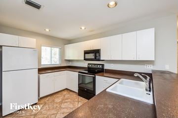 Fort Myers house for rent - a kitchen with white cabinets and a sink and a refrigerator