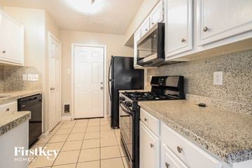 Houston house for rent - a kitchen with white cabinets and black appliances and granite counter tops