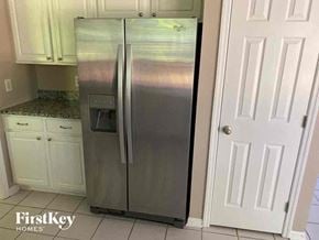 Loveland house for rent - A stainless steel refrigerator stands in a kitchen with white cabinets and a white door.