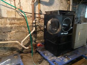Buffalo apartment for rent - A large black boiler with two glass windows is on a blue platform in a room with pipes.