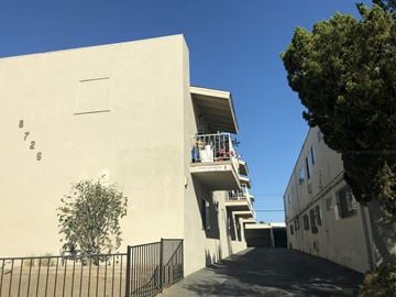 Canoga Park apartment for rent - A white building with a black fence and a tree in front of it.