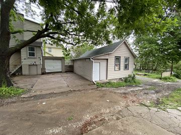 Omaha apartment for rent - A small house with a garage is surrounded by trees and vegetation.