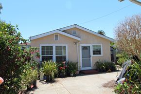 Alameda apartment for rent - A small house with a white door and windows surrounded by plants.