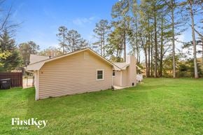 Austell house for rent - A house with a brown roof and a beige siding is surrounded by a grassy lawn and trees.