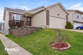 Arnold house for rent - A house with a brown and beige exterior is shown with a small tree in a circular flower bed in the front yard.
