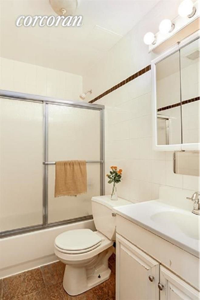 Brooklyn apartment for rent - A white toilet sits in a bathroom with a white sink and a brown towel hanging on the glass shower door.