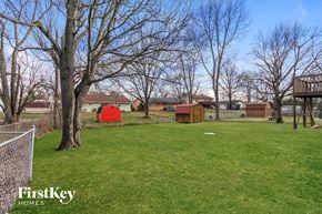 Mason house for rent - A grassy field with trees and a fence with a house in the background.