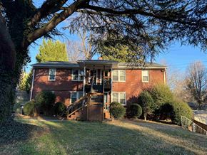Winston Salem apartment for rent - A red brick house with a porch and a tree in front.