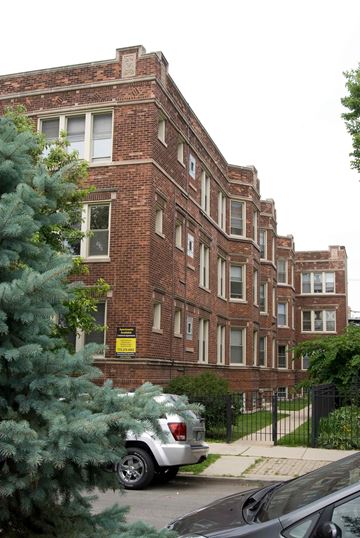 Chicago apartment for rent - A building with a black fence and a tree in front of it.