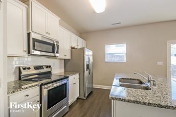 Charlotte house for rent - A kitchen with a stove top oven, microwave, refrigerator, and sink.