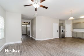 Charlotte house for rent - A spacious room with a ceiling fan and light fixture, and a kitchen area with a refrigerator and cabinets.