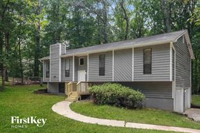 Douglasville house for rent - A house with a grey siding and a white door is surrounded by greenery.