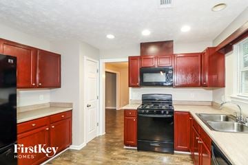 Buford house for rent - a kitchen with red cabinets and black appliances and a sink