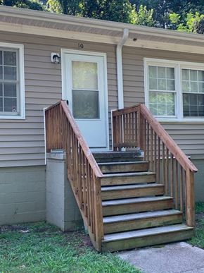 Raleigh apartment for rent - A house with a grey siding and a white door has a wooden staircase leading to the front door.