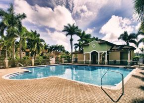 Homestead apartment for rent - A pool surrounded by palm trees and a house.