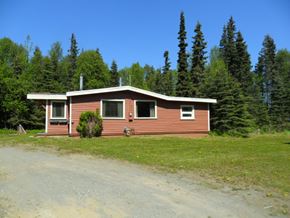 Kenai apartment for rent - A house with a brown roof and a brown fence is surrounded by trees.