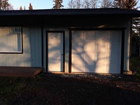 Soldotna house for rent - A small building with a white garage door and a brown bench in front.