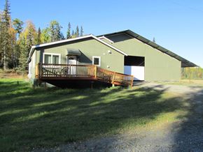 Soldotna apartment for rent - A green house with a deck in the middle of a grassy field.