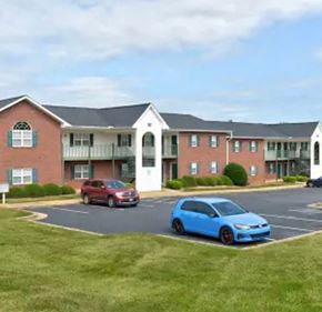 Youngsville apartment for rent - A blue car is parked in a parking lot in front of a red car and a building.