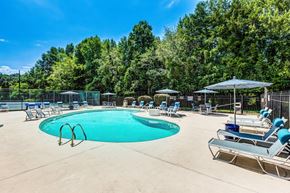 Concord apartment for rent - A large outdoor swimming pool surrounded by trees and lounge chairs.