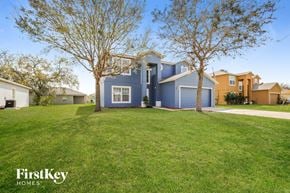 Poinciana house for rent - a blue house with a lawn and trees in front of it