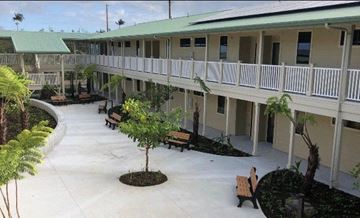 Hilo apartment for rent - A courtyard with benches and trees in front of a building.
