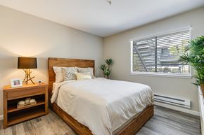 Hayward apartment for rent - A bedroom with a large bed, a nightstand with a lamp, and a window with blinds.
