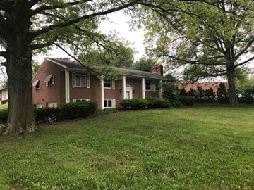 North Canton apartment for rent - A house with a red brick exterior and a white trim is surrounded by a well-manicured lawn and trees.