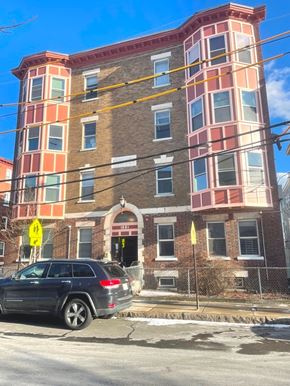 Cambridge apartment for rent - A car is parked in front of a multi-story building with a yellow warning sign on the sidewalk.