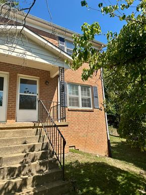 Charlottesville apartment for rent - A house with a brick facade and a white door is surrounded by greenery.