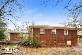 Powder Springs house for rent - A brick house with a white door and windows is surrounded by trees and grass.