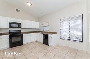 Orlando house for rent - a kitchen with white cabinets and black appliances and a large window