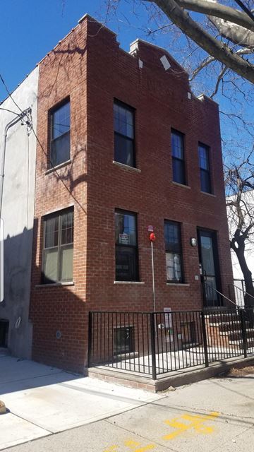 Brooklyn apartment for rent - A red brick building with a black iron fence in front.