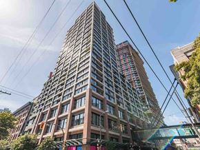 Vancouver apartment for rent - A tall building with many windows is surrounded by trees and other buildings.